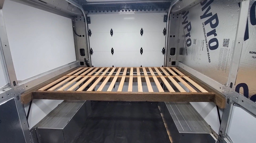 Slatted timber bed platform framed across a van interior with storage underneath