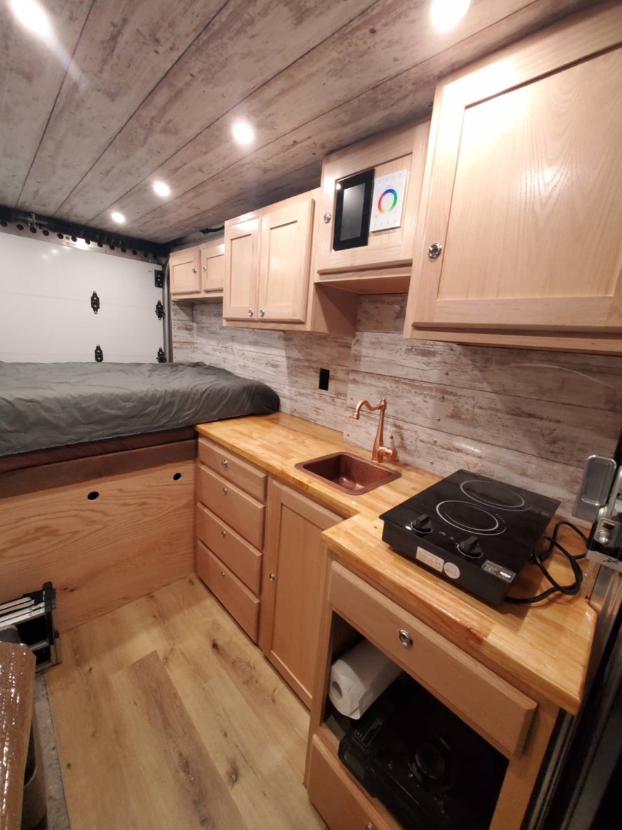 Finished van galley with butcher block counter, sink, induction cooktop and cabinets